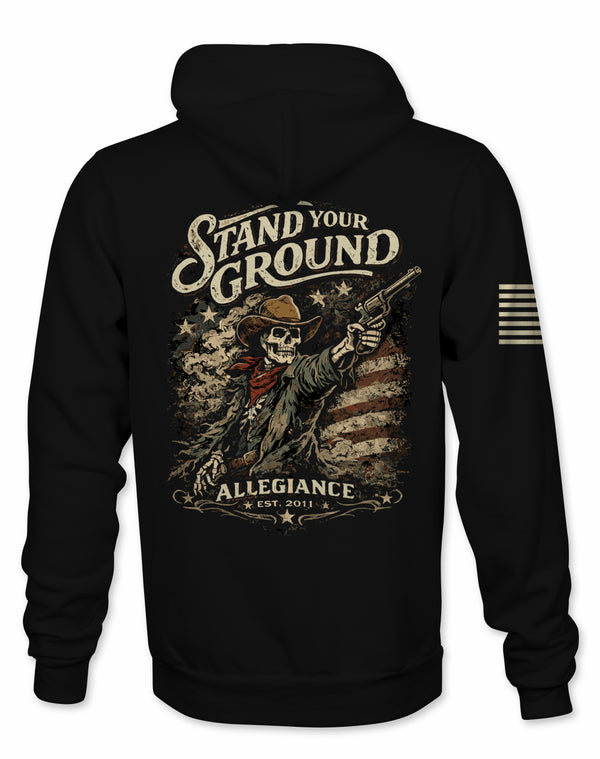 A black pullover hoodie shown from the back, featuring a large distressed graphic print of a skeleton cowboy holding a revolver with the text 'Stand Your Ground' and 'Allegiance Est. 2011'.